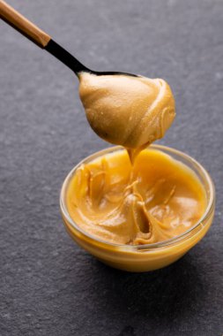 Gri yüzeyde fıstık ezmeli kaşık ve kâsenin dikey görüntüsü. Yiyecek, kahvaltı, beslenme ve Amerikan mutfağı konsepti.