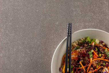 Gri arka planda fotokopi alanı olan Asyalı tava kızartma ve yemek çubuklarının genel görünümü. Asyalı lezzetli ev yemekleri ve sağlıklı yiyecekler..