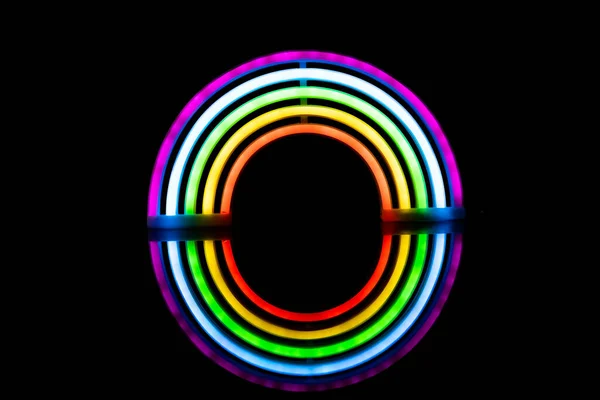 Image of vibrant neon glow sticks forming rainbow with reflection on black background and copy space. Lgbt, equality, love, light and colour concept.