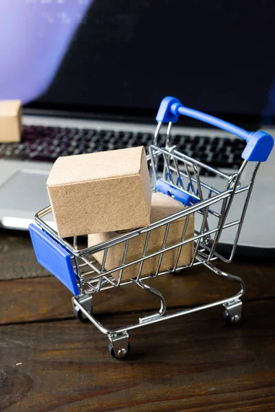 Composition of shopping cart with boxes and laptop on wooden background. Retail, shopping and black friday concept.