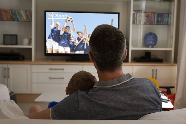 Rear view of father and son sitting at home together watching football match on tv. sports, competition, entertainment and technology concept digital composite image.