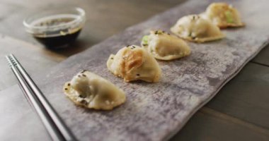 Tabakta gyoza köftesi ve soya sosuyla ahşap arka planda yemek çubukları var. Yiyecek, içecek ve renk konsepti.