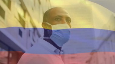 Kolombiya bayrağının şehir caddesinde maskeli Afro-Amerikan bir adamın üzerinde sallanışının animasyonu. covid 19 salgın konsepti boyunca dijital olarak üretilen küresel sağlık önlemleri.