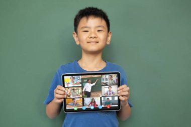 Çeşitli ilkokul öğrencileriyle video görüşmesi için elinde tablet olan gülümseyen Asyalı çocuk. iletişim teknolojisi ve çevrimiçi eğitim, dijital kompozit resim.
