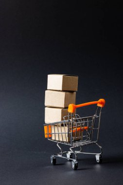 Kutuları olan alışveriş arabasının kompozisyonu ve gri arka planda kopyalama alanı. Perakende, alışveriş ve Kara Cuma konsepti.