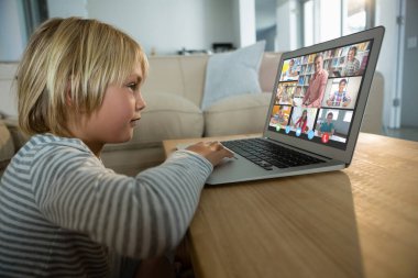 Beyaz çocuk ekranda çeşitli ilköğretim öğrencileri gülümserken görüntülü konuşma için laptop kullanıyor. iletişim teknolojisi ve çevrimiçi eğitim, dijital kompozit resim.