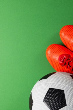 Fotokopi alanı olan yeşil arka planda futbol ve kırmızı ayakkabıların kompozisyonu. Spor, hareket, eğitim ve aktif yaşam tarzı kavramı.