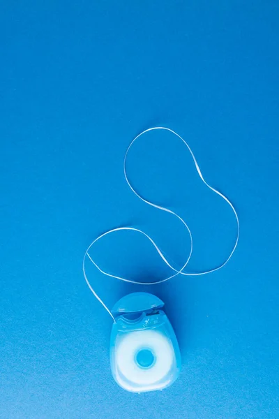 Vertical image of dental string on blue surface. Health, dentistry, dental accessories and taking care of teeth concept.