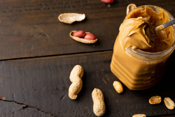 Image of jar with peanut butter and nuts on wooden surface. Food, breakfast, nutrition and american cuisine concept.