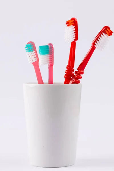 Vertical image of toothbrushes in cup on grey background. Health, dentistry, dental accessories and taking care of teeth concept.