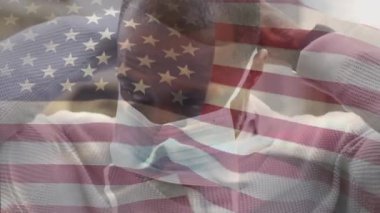Amerikan bayrağının şehir caddesinde maskeli Afro-Amerikan bir adamın üzerinde dalgalanmasının animasyonu. covid 19 salgın konsepti boyunca dijital olarak üretilen küresel sağlık önlemleri.