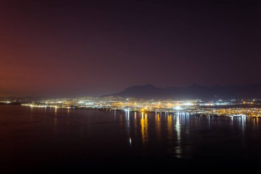 Deniz manzarası, deniz kıyıları şehir ışıkları, dağlar, gece ve ufukta bulutsuz gökyüzü. Manzara, deniz ve doğa kavramı.