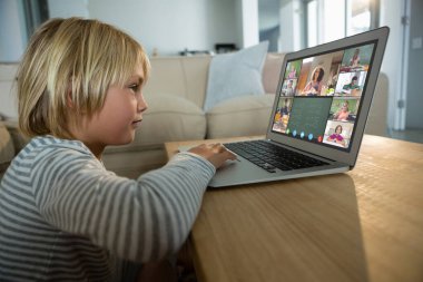 Beyaz çocuk ekranda çeşitli ilköğretim öğrencileri gülümserken görüntülü konuşma için laptop kullanıyor. iletişim teknolojisi ve çevrimiçi eğitim, dijital kompozit resim.