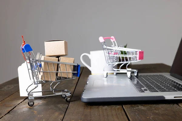 Composition of shopping carts with boxes and laptop on gray background. Retail, shopping and black friday concept.