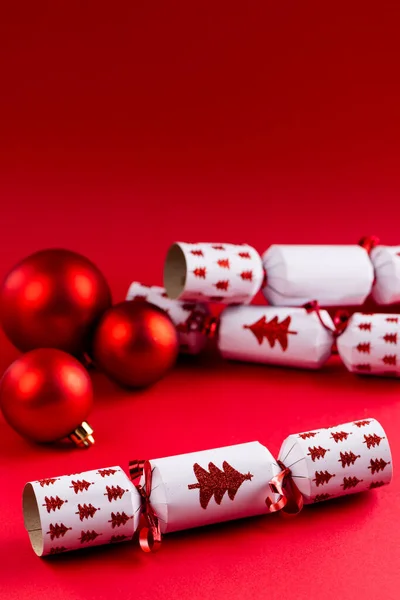 Image of christmas crackers with christmas baubles on red background. Christmas, tradition and celebration concept.