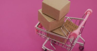 Kartondaki kara Cuma metinlerinin videosu ve pembe arka plandaki alışveriş arabasındaki kutular. Kara Cuma, perakende, alışveriş ve tasarruf kavramı.