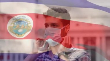 Costarica bayrağının şehir caddesinde yüz maskesi takan Latin adamın üzerinde dalgalanması. covid 19 salgın konsepti boyunca dijital olarak üretilen küresel sağlık önlemleri.