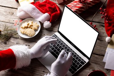Noel Baba 'nın elleri boş ekranlı dizüstü bilgisayar kullanırken ve tahta arka planda boşluk kopyalarken görüntüsü. Noel, bağlantı, teknoloji, gelenek ve kutlama konsepti.