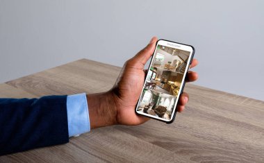 Beyaz perdedeki güvenlik kameralarından evi gören akıllı telefonu tutan Afro-Amerikan bir adamın eli. güvenlik, güvenlik, izleme ve dijital arayüz.