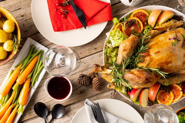Overhead view of thanksgiving table with roast chicken and vegetables and autumn decoration on wood. Thanksgiving, autumn, fall, american tradition and celebration concept.