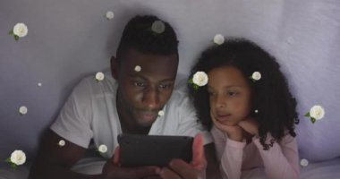 Mutlu Afro-Amerikan baba ve kızının yatakta tablet kullanması üzerine gül animasyonu. Aile hayatı, çocukluk, aşk ve bakım konsepti dijital olarak oluşturulmuş video.