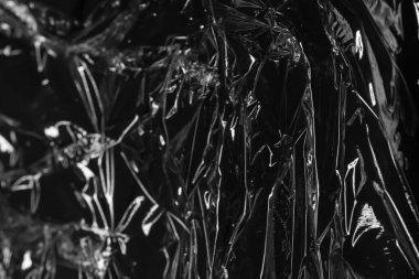 Kırışıklıklar ve kıvrımlar üzerindeki ışığı ve gölgeyi siyah plastik kaplamayla yansıtıyor. monokrom ışık ve doku, soyut arkaplan resmi.