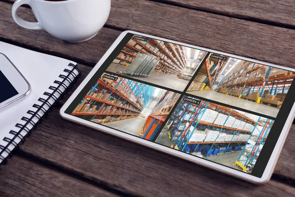 Tablet with views of warehouse from security cameras on screen lying on wooden table. security, safety, surveillance, and digital interface.