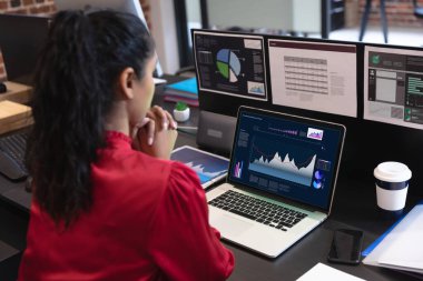 Çift ırklı iş kadını masada oturuyor ve ekranında istatistiksel veriler olan bir dizüstü bilgisayar kullanıyor. iş iletişimi ve dijital arayüz teknolojisi dijital kompozit görüntü.