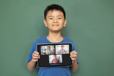 Çeşitli ilkokul öğrencileriyle video görüşmesi için elinde tablet olan gülümseyen Asyalı çocuk. iletişim teknolojisi ve çevrimiçi eğitim, dijital kompozit resim.