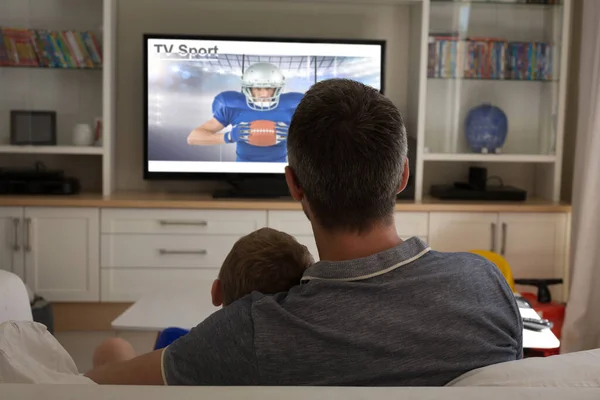 Rear view of father and son sitting at home together watching sport event on tv. sports, competition, entertainment and technology concept digital composite image.