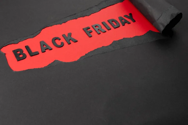 Composition of black paper and black friday text on red background. Retail, shopping and black friday concept.