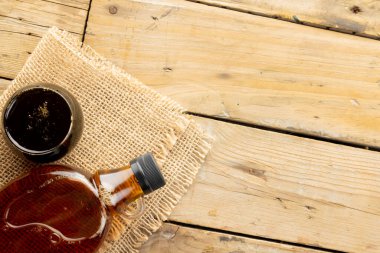 Cam şişenin yatay görüntüsü ve tahta masadaki çuval bezin üzerine akçaağaç şurubu. Kopya alanı. Yiyecek, organik malzemeler ve sağlıklı yiyecekler..