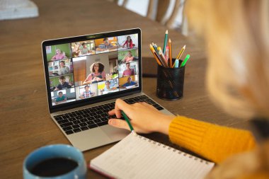Beyaz bir kadın ekranda çeşitli ilkokul öğrencilerinin gülümsediği bir video görüşmesi için dizüstü bilgisayar kullanıyor. iletişim teknolojisi ve çevrimiçi eğitim, dijital kompozit resim.