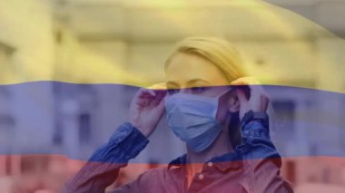 Kolombiya bayrağının şehir caddesinde yüz maskesi takan beyaz bir kadının üzerinde dalgalanması. covid 19 salgın konsepti boyunca dijital olarak üretilen küresel sağlık önlemleri.