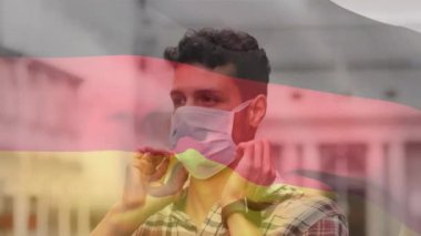 Alman bayrağının şehir caddesinde maske takan latin adamın üzerinde dalgalanmasının animasyonu. covid 19 salgın konsepti boyunca dijital olarak üretilen küresel sağlık önlemleri.