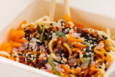 Asya tavasını yakın çekimde, kağıt kutuda çubuklarla erişte kızartır. Asyalı lezzetli ev yemekleri ve sağlıklı yiyecekler..