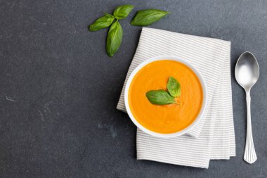Fesleğen yapraklı, kaşık ve peçeteli domates çorbasının yatay görüntüsü. Lezzetli ev yemekleri ve sağlıklı yemekler..