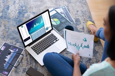 Çift ırklı iş kadını ekranda istatistiksel verileri olan bir dizüstü bilgisayar kullanarak yerde oturuyor. iş iletişimi ve dijital arayüz teknolojisi dijital kompozit görüntü.