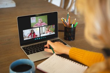 Beyaz bir kadın ekranda çeşitli ilkokul öğrencilerinin gülümsediği bir video görüşmesi için dizüstü bilgisayar kullanıyor. iletişim teknolojisi ve çevrimiçi eğitim, dijital kompozit resim.