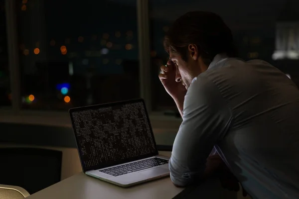 Caucasian male programmer sitting at desk, using laptop with coding on screen. coding, programming and computer technology digital composite image.