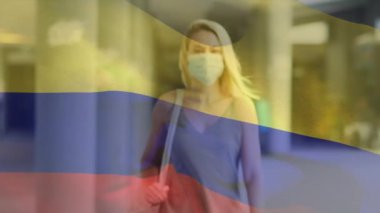 Kolombiya bayrağının şehir caddesinde yüz maskesi takan beyaz bir kadının üzerinde dalgalanması. covid 19 salgın konsepti boyunca dijital olarak üretilen küresel sağlık önlemleri.
