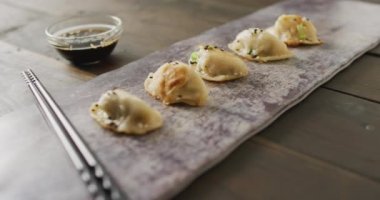 Tabakta gyoza köftesi ve soya sosuyla ahşap arka planda yemek çubukları var. Yiyecek, içecek ve renk konsepti.