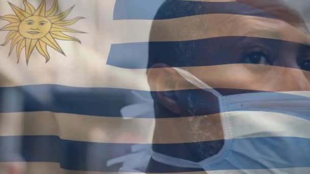 Animación Bandera Uruguay Ondeando Sobre Hombre Afroamericano Con Máscara Facial — Vídeo de stock