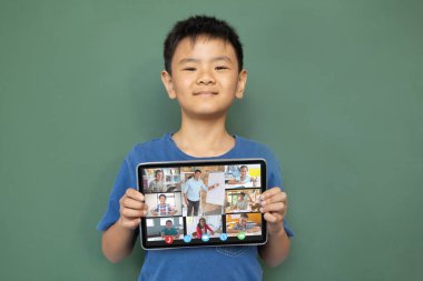Çeşitli ilkokul öğrencileriyle video görüşmesi için elinde tablet olan gülümseyen Asyalı çocuk. iletişim teknolojisi ve çevrimiçi eğitim, dijital kompozit resim.