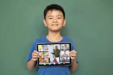 Çeşitli ilkokul öğrencileriyle video görüşmesi için elinde tablet olan gülümseyen Asyalı çocuk. iletişim teknolojisi ve çevrimiçi eğitim, dijital kompozit resim.