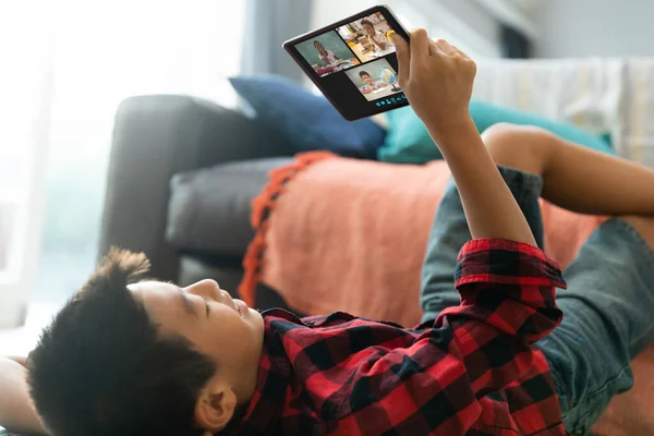 ビデオ通話用のタブレットを持っているアジアの少年を笑顔 画面上の多様な小学生と 通信技術とオンライン教育デジタル複合画像 — ストック写真