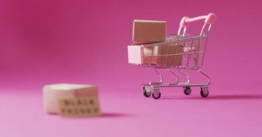 Kartondaki kara Cuma metinlerinin videosu ve pembe arka plandaki alışveriş arabasındaki kutular. Kara Cuma, perakende, alışveriş ve tasarruf kavramı.