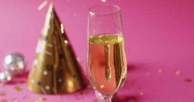 Pembe arka planda altın renkli parti şapkalı ve takı takan iki şampanya kadehinin videosu. Yeni yıl partisi ve kutlama konsepti.