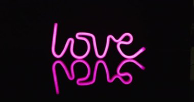 Siyah arkaplanda aşk metni oluşturan pembe neon ışıkların animasyonu. Arkaplan, telif alanı ve renk kavramı.