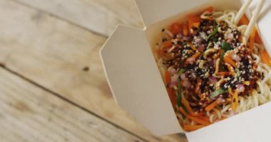 Tahta arka planda yemek çubukları olan bir kutu Tayland yemeği. Yiyecek, içecek ve renk konsepti.